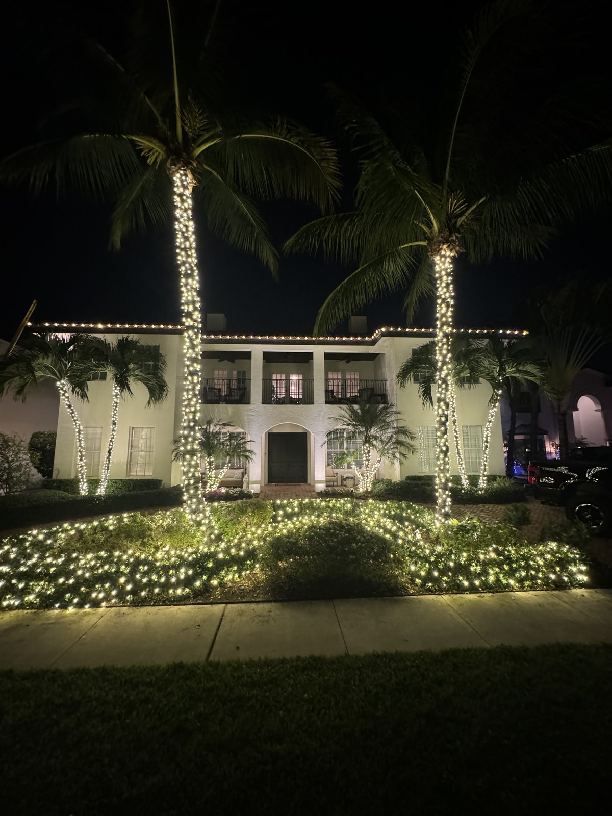 Gulfstream Glow palm trees wrapped in lights at a two-story estate entry