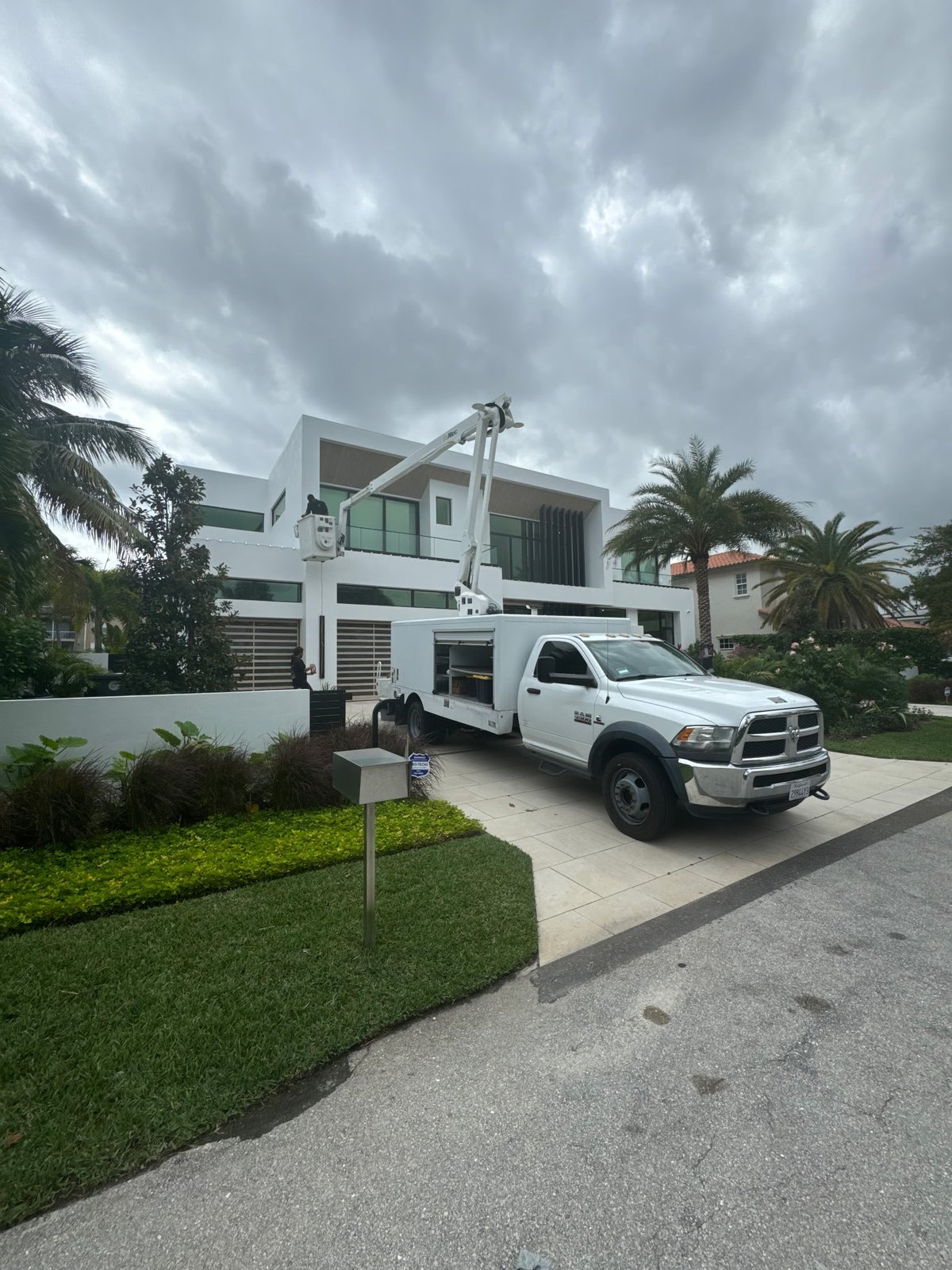Gulfstream Glow bucket truck lighting palms at a modern home on a cloudy day