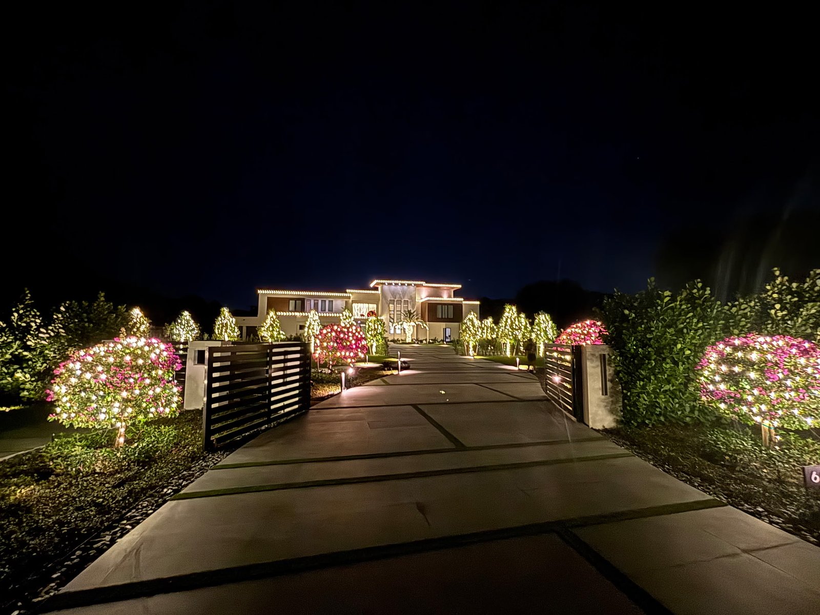 Gulfstream Glow lit driveway entrance with bougainvillea hedges and a glowing palm